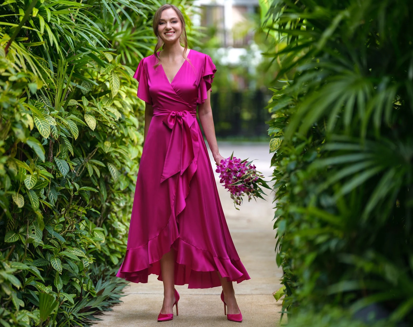 Rochie din satin fucsia cu volane și cordon, într-un decor tropical
